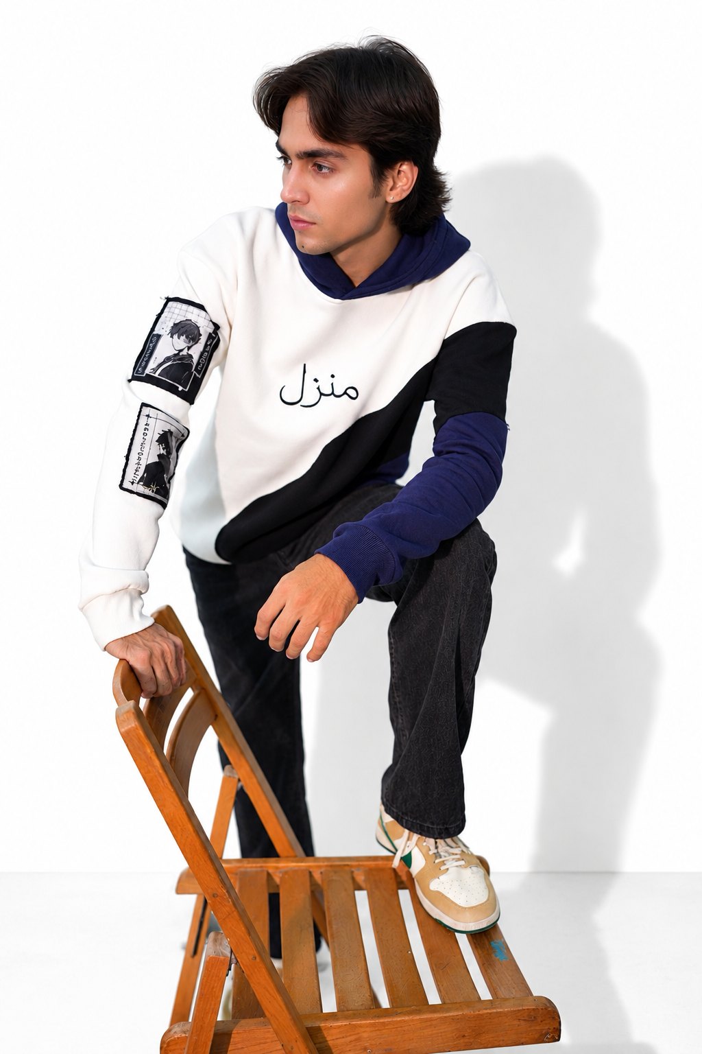 Manzil navy and white colour-block hoodie with Urdu print, model posing with one foot on a wooden chair